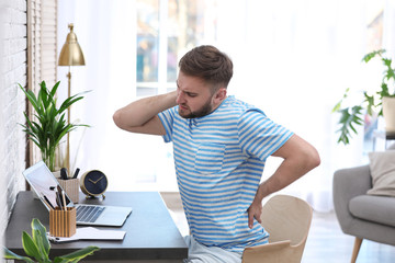 Young man suffering from back pain in office