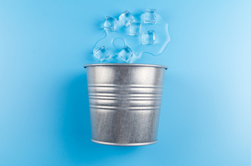 melting ice and metal bucket on blue background