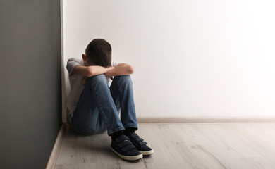 Upset boy sitting on floor indoors. Space for text
