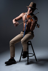 Fototapeta na wymiar Thw handsome man show body muscle ,sitting on black chair,playing violin with happy feeling,vintage and art tone