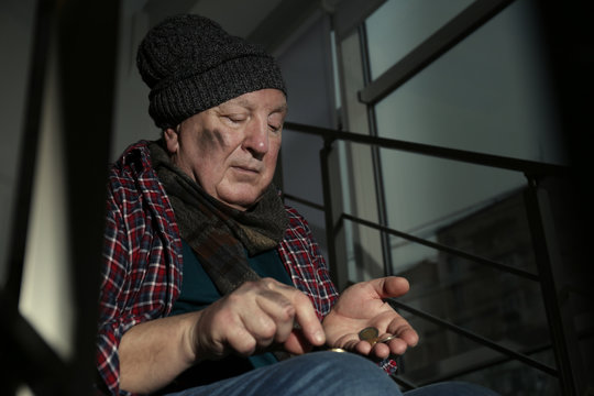 Poor Senior Man Counting Coins On Stairs Indoors. Space For Text