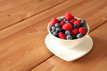 Ripe sweet different berries in white bowl on rustic wooden table. Harvest Concept