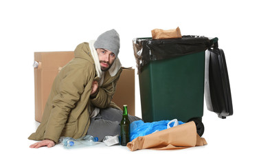 Poor homeless man sitting near trash bin isolated on white