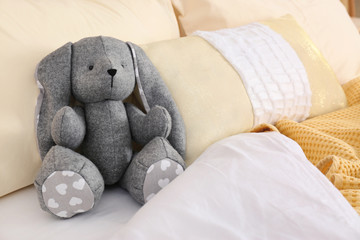 Cute toy rabbit on bed in child's room interior. Space for text
