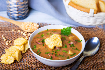 Peas soup with meat, smoked sausage and croutons. Selective focus, close-up.