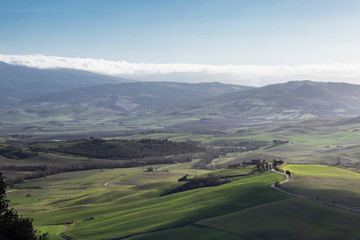 Green typical Tuscany landscape in Italian region with fields, meadow, hills and path with farmhouses