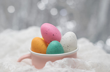 Easter eggs in a pink cup, on white lace with a soft bokeh background