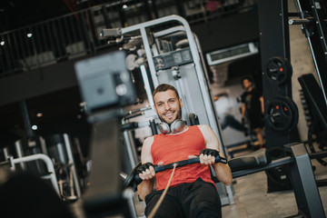 Young man doing workouts on a back with power exercise machine in a gym club