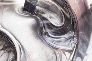 Close-up on the tank with silver black paint while mixing with spiral patterns in the painting and art workshop