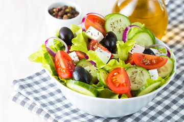 Fresh Greek salad made of cherry tomato, ruccola, arugula, feta, olives, cucumbers, onion and spices. Caesar salad in a white bowl on wooden background. Healthy organic diet food concept.