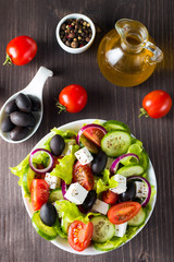 Fresh Greek salad made of cherry tomato, ruccola, arugula, feta, olives, cucumbers, onion and spices. Caesar salad in a white bowl on wooden background. Healthy organic diet food concept.