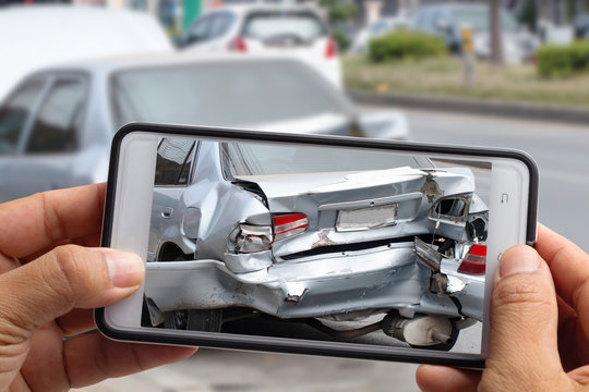 Car insurance agents take pictures of accident-damaged vehicles with a smartphone.