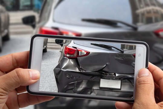 Car insurance agents take pictures of accident-damaged vehicles with a smartphone.