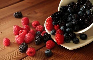 Ripe sweet different berries in white bowl on rustic wooden table. Harvest Concept