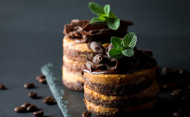 Chocolate cakes on black slatter board with mint, coffee beans on dark background, closeup photo. Fresh, tasty dessert food concept. 