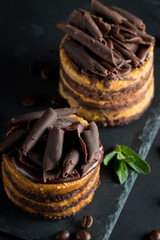 Chocolate cakes on black slatter board with mint, coffee beans on dark background, closeup photo. Fresh, tasty dessert food concept. 