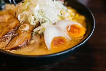 Close up Ramen Pork Bone Soup (Tonkotsu Ramen) with Chashu Pork, Scallion, Sprout, Corn, Dried Seaweed and boiled egg served in black bowl.