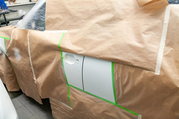 The car rear view after the accident in the camera for car body repair is partially covered with paper and pasted over with green masking tape for painting the side doors with white