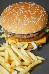 Close-up of a delicious fresh hamburger with lettuce, cheese and onions and fries on a dark background
