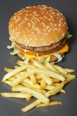 Close-up of a delicious fresh hamburger with lettuce, cheese and onions and fries on a dark background