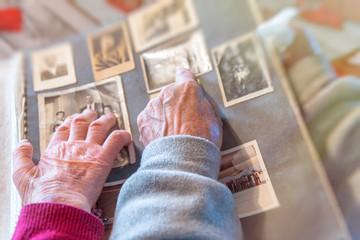 Elderly couple hands looking at old pictures album at home. Detail on hands and old images