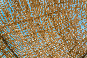 Lonely wicker sun umbrella at mediterranean beach by sea. Natural bamboo sunshades and summer umbrella parasol on ocean beach. Large straw beach umbrellas against blue water and sky. Vacation, travel.