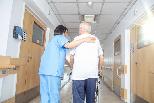 Asian female doctor reassuring mature elderly man with walker. Man and woman smiling happy in the hospital aisle. Retirement community concept