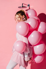 Fototapeta na wymiar happy beautiful young woman holding air balloons while standing on pink