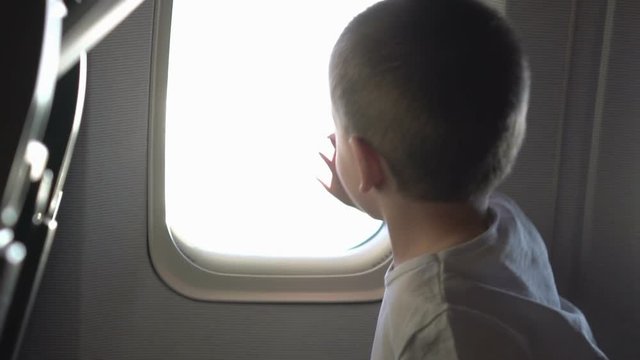 Young cute boy sitting on the seat and opens up airplane window