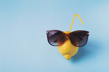 Lemon fruit in sunglasses on blue background, vacation concept