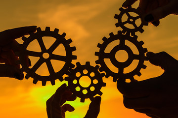 Gears in the hands of people on the background of the evening sky. teamwork, interaction.