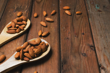 Almonds in a glass bowl and wooden spoons on grained wood background.