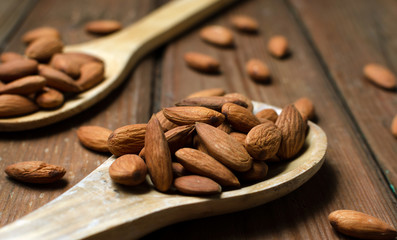 Almonds in a glass bowl and wooden spoons on grained wood background.