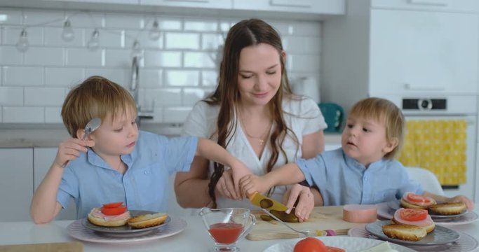 Beautiful young mother with two children sons on white light kuna cook with burgers