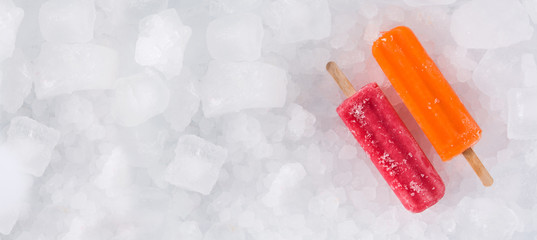 Orange and strawberry popsicles on ice cubes. Panoramic view