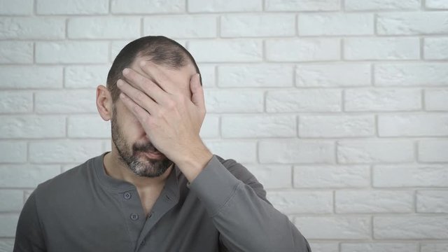 The man is at a loss. A man in despair covers his face with his hand.