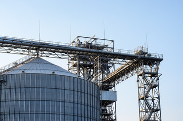 Fototapeta na wymiar Large silo (huge metal tank for sugar, grain or silage storage) and other industrial equipment of modern sugar plant: metal structures and tower