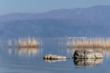 Rocks in the lake with a background of mountains and blue sky.