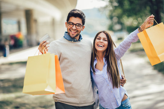 Portrait of happy couple with shopping bags after shopping in city smiling and holding credit card