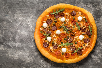 pizza with mozzarella, capers, tomatoes and arugula on a concrete background