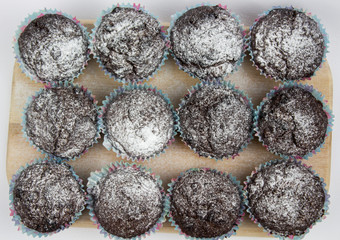 Chocolate-banana Muffins with sugar powder on a wooden board on a white background. View from above. Copy space