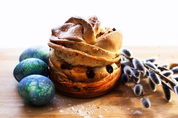 Still-life with festive pastries with raisins and nuts, dusted with sugar, dyed blue eggs and willow blossoms. Breakfast on a wooden board. Close-up, isolated.