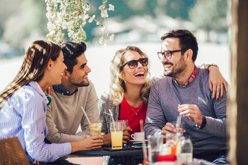 Group of four friends having fun a coffee together. Two women and two men at cafe talking laughing and enjoying their time