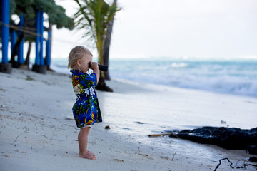 Sweet boy looks through binoculars, observating the ocean life and waves
