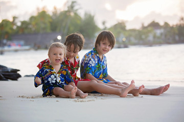 Happy beautiful fashion family, children, dressed in hawaiian shirts, playing together on the beach on sunset