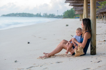 Fototapeta premium Happy beautiful fashion family, mom and baby, hugging, casually dressed, enjoying the sunrise on the beach in Mauritius