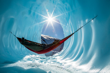 Ice climber rests in hammock inside ice cave in the Alaskan wilderness