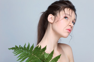 Beautiful  girl with fern leaf, isolated on a light - grey  background, emotions, cosmetics