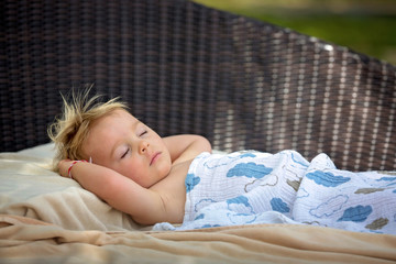 Cute blond toddler boy, sleeping on a big round beach chair on the deck of pool next to the beach on tropical island