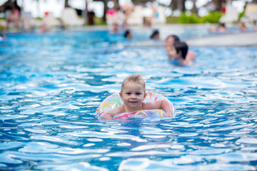 Fototapeta na wymiar Adorable happy little child, toddler boy, having fun relaxing and playing in a pool in inflatable ring on sunny day during summer vacation